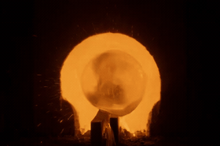 Molten glass blown into a bulb over an orange furnace